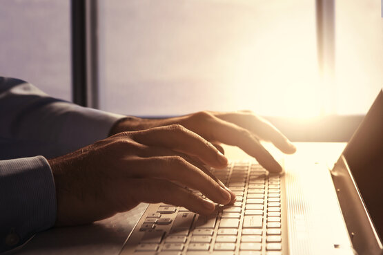 Person tippt mit beiden Händen auf Laptop-Tastatur, heller Hintergrund