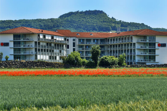 Modernes Hauptgebäude der Schön Klinik Bad Staffelstein im Grünen, umgeben von blühenden Wiesen, Feldern und Hügeln