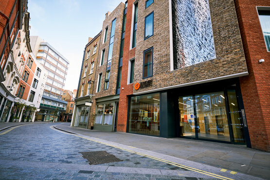 Mehrstöckiges Backsteingebäude mit großen Fenstern und gläsernem Eingang, Schön Klinik London an schmaler Stadtstraße
