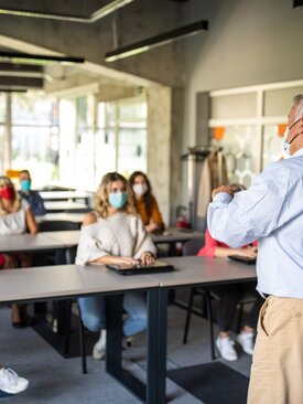 Lehrer unterrichtet Schüler mit Masken in modernem, hellem Seminarraum