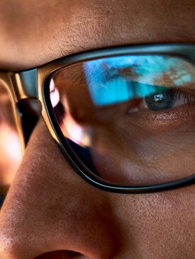 Nahaufnahme von Augen hinter schwarzer Brille mit Monitor-Reflexion