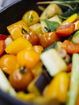 Bunte, geschnittene Gemüse wie gelbe Paprika, Tomaten, Zucchini, Aubergine und Frühlingszwiebeln in schwarzer Pfanne