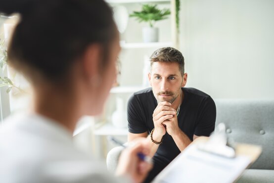 Therapeutisches Gespräch in moderner Klinik: Patient sitzt nachdenklich auf Sofa, Therapeutin hört empathisch zu.