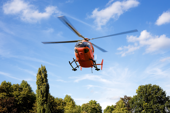Rettungshubschrauber im Landeanflug bei sonnigem Wetter über grüner Parklandschaft