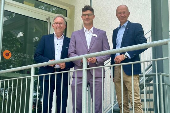 Drei Männer im Anzug stehen vor dem Eingang der Schön Klinik Bad Arolsen bei einem offiziellen Besuch