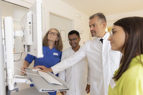 Ärzteteam und Pflegepersonal bei Visite betrachten gemeinsam Patientendaten am Computer