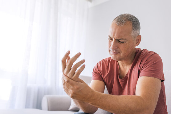 Mann hält sich mit schmerzverzerrtem Gesicht das rechte Handgelenk, Fokus auf Hand und Gesichtsausdruck