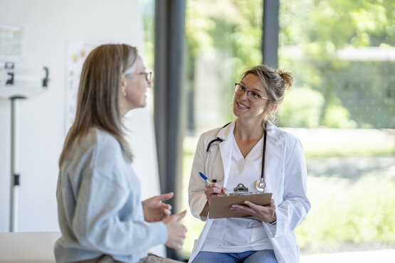 Ärztin im weißen Kittel führt ein Beratungsgespräch mit Patientin in heller Praxis