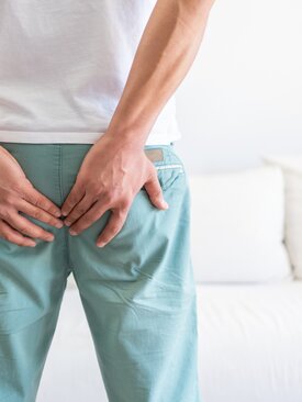 Person von der Hüfte abwärts legt beide Hände auf das Gesäß