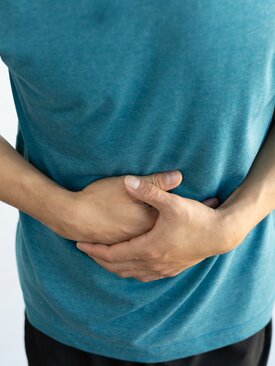 Person in blauem T-Shirt hält sich den Bauch mit beiden Händen