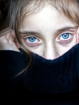 Kind mit hellbraunen Haaren zieht angespannt den Pullover am Gesicht hoch
