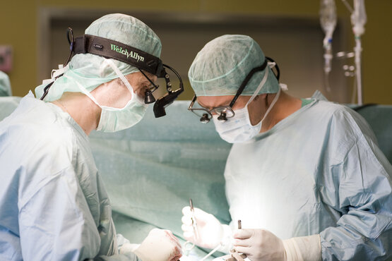 Zwei Chirurgen in OP-Kleidung und Mundschutz operieren konzentriert im modernen, gut beleuchteten Operationssaal