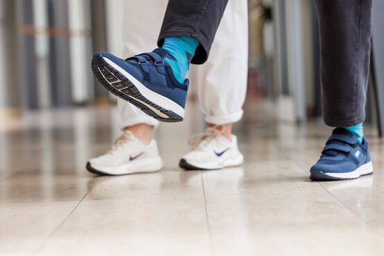 Zwei Personen gehen im Klinikflur, Fokus auf Antifreezingschuh und Nike-Sneaker.