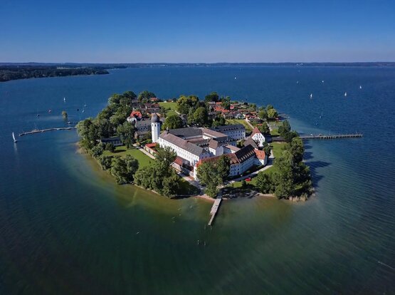 Luftaufnahme der Fraueninsel im Chiemsee mit Klosteranlage, Wohnhäusern und Segelbooten auf blauem Wasser.