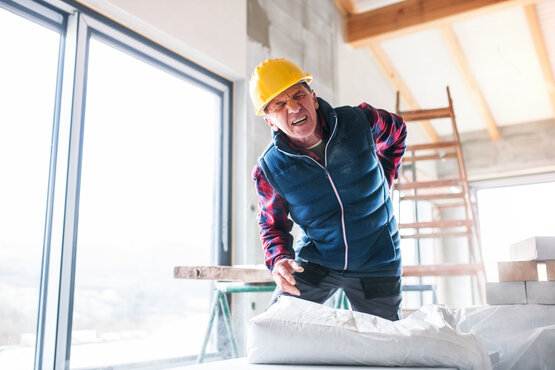 Bauarbeiter mit Schutzhelm hält sich schmerzhaft den Rücken im Rohbau