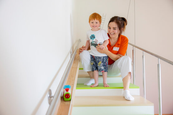 Therapeutin unterstützt Jungen beim Treppensteigen in der Kinderrehabilitation