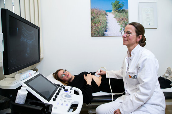 Ärztin in weißem Kittel führt Ultraschalluntersuchung des Bauches bei Patientin in Klinik durch, Monitor zeigt Ultraschallbild